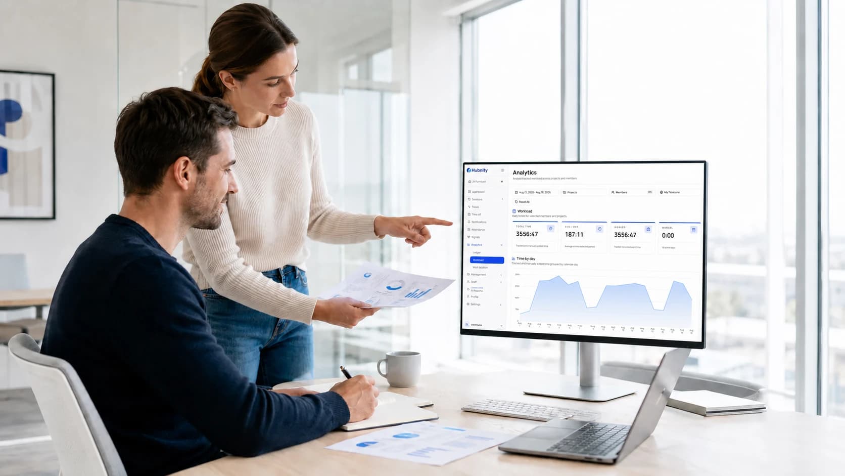 Colleagues reviewing a Hubnity time report on a monitor